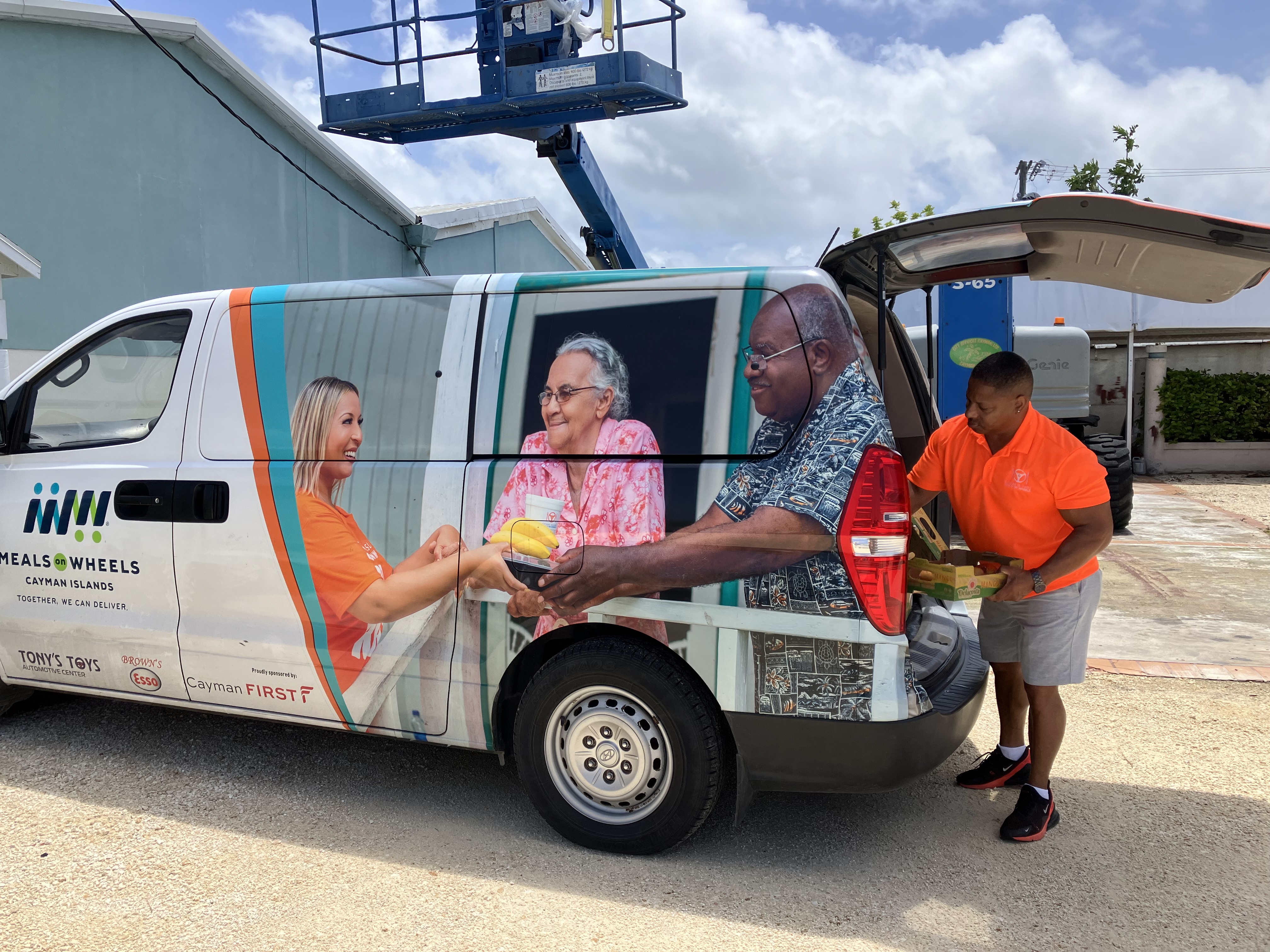 a man taking a pallet of food off a Meals On Wheels Cayman Van 