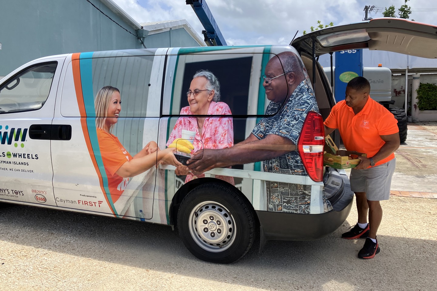 a man taking a pallet of food off a Meals On Wheels Cayman Van
