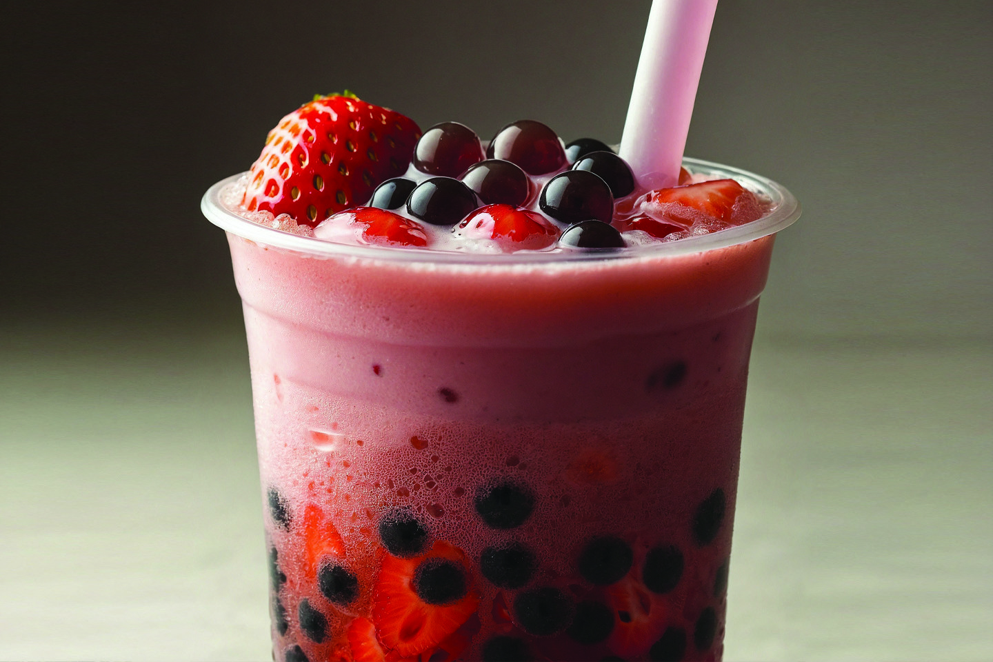 Bubble tea with strawberries and a straw in a clear plastic cup