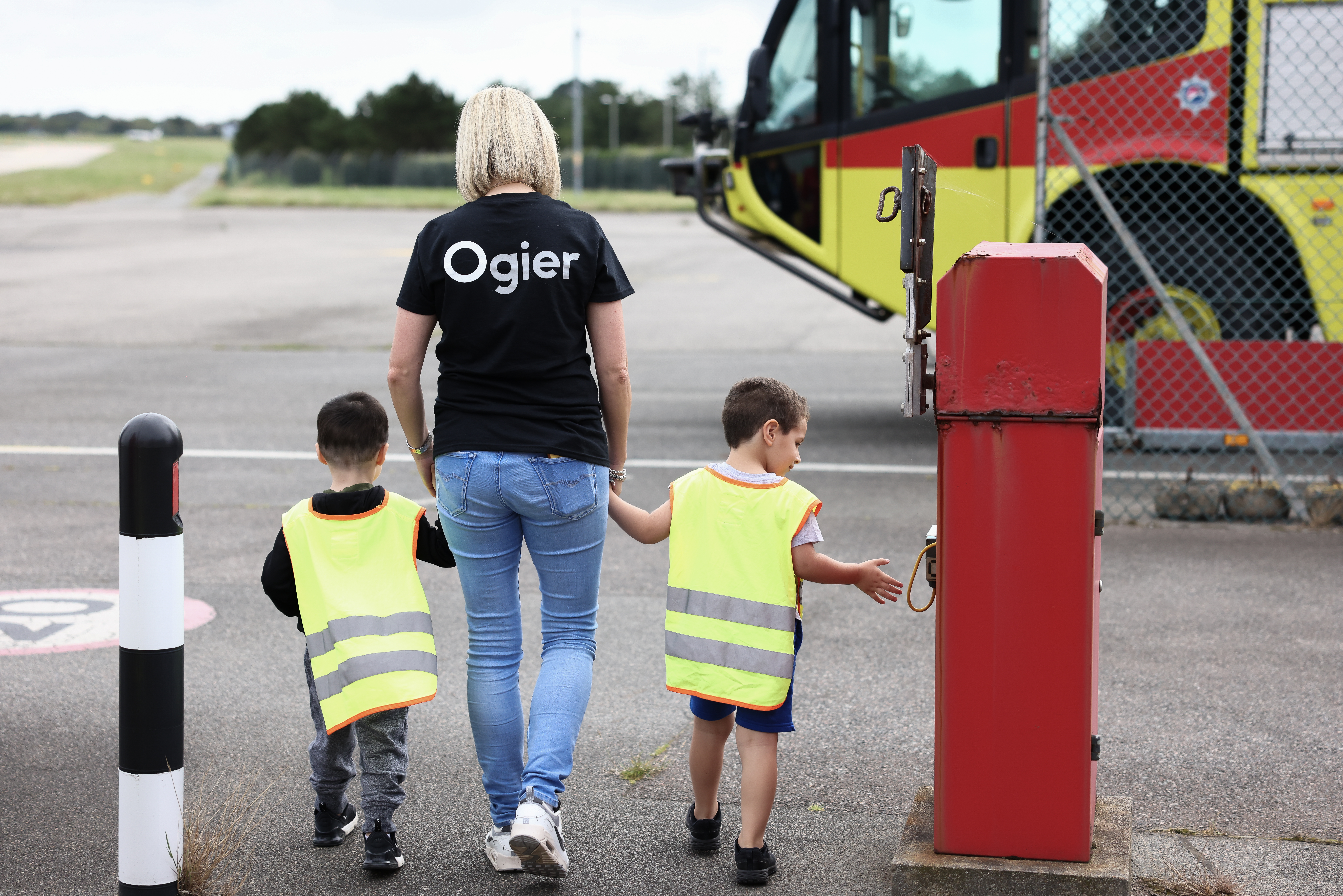 Ogier team member walks with two preschool children in high-visibility vests near an airport fire engine