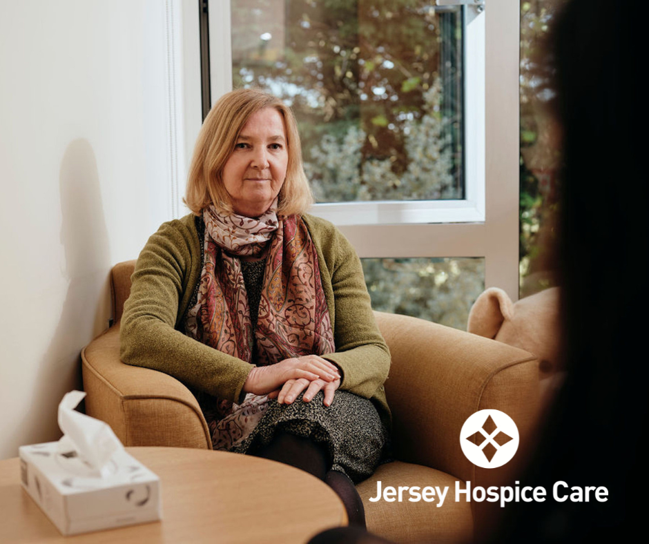 older individual sits in a welcoming room at Jersey Hospice Care, with the charity logo displayed in white.