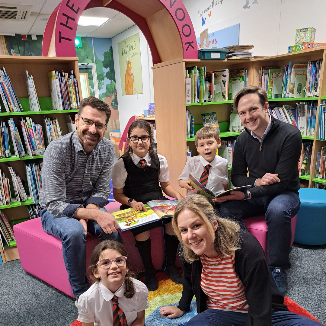 group of adults and school children enjoying storytelling together in a colourful library at Rouge Bouillon School in Jersey.