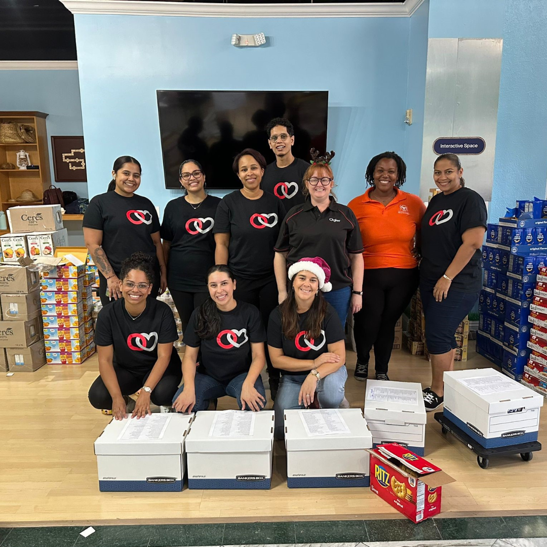 volunteers in Ogier shirts and Meals on Wheels staff assemble and pack 225 Christmas grocery boxes for delivery to vulnerable residents in Grand Cayman.